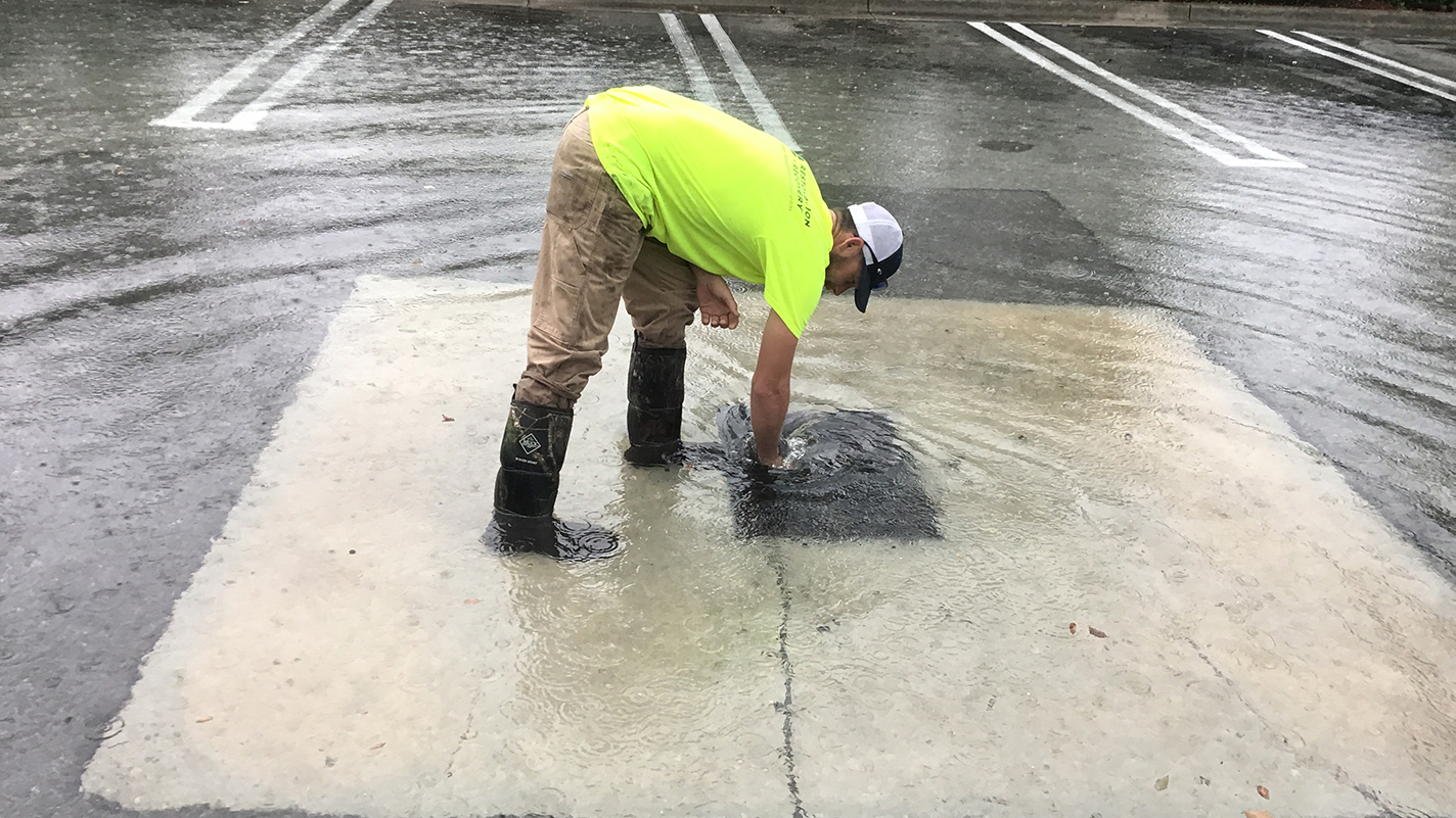 flooding parking lot with man trying to unclog the storm drain from above