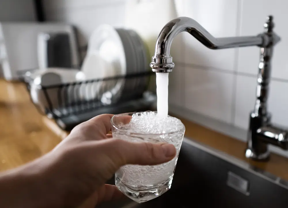 potable water and safe to drink. man filling a glass of water from a stainless steel kitchen tap. male's hand pouring water into the glass from chrome faucet to drink running water with air bubbles.