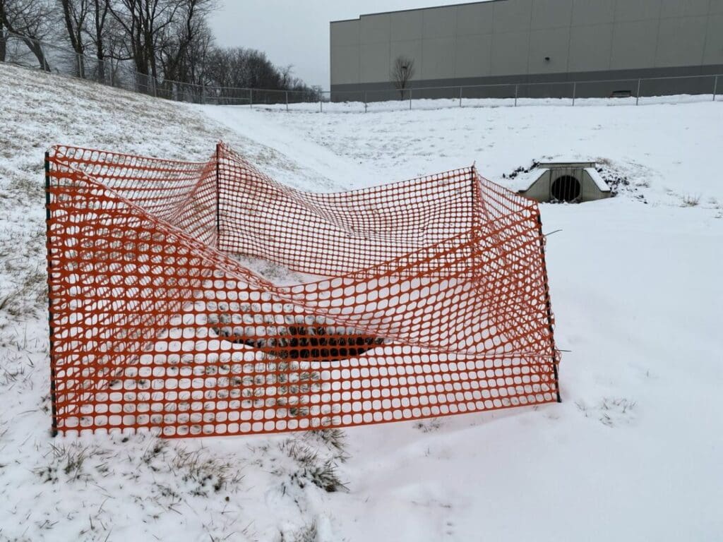 sinkhole in the snow being guarded off by orange fencing